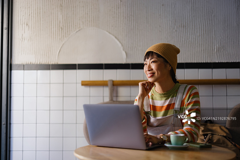 年轻女性在咖啡店用笔记本电脑远程工作时微笑图片素材