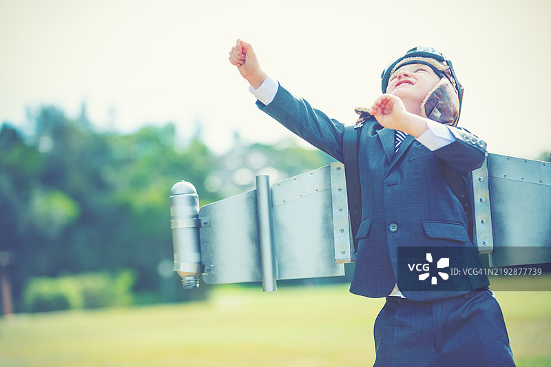 抱负、创新商业理念。一个穿着西装和自制传统飞行员服装的小孩。图片素材
