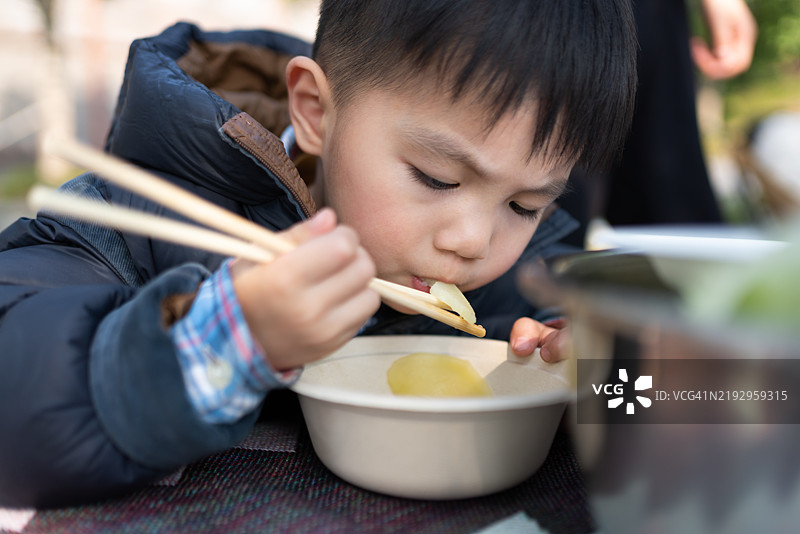 一个亚洲学龄前儿童在户外用筷子吃饭图片素材