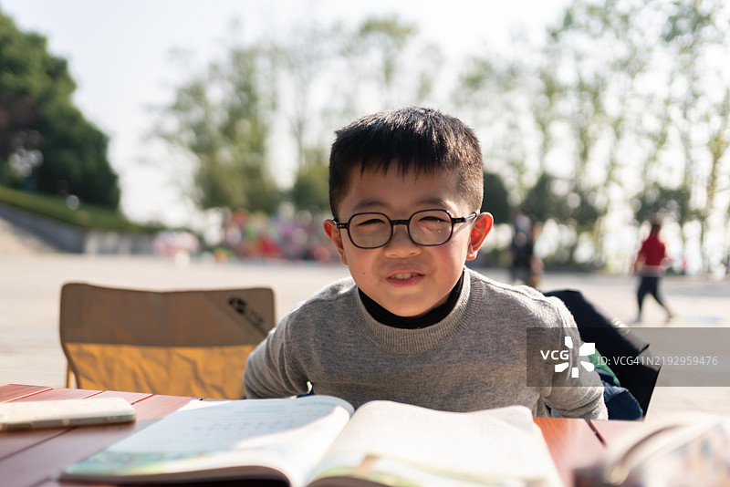 一名戴着近视眼镜的亚洲小学生正在做作业，开心地面对着镜头。图片素材