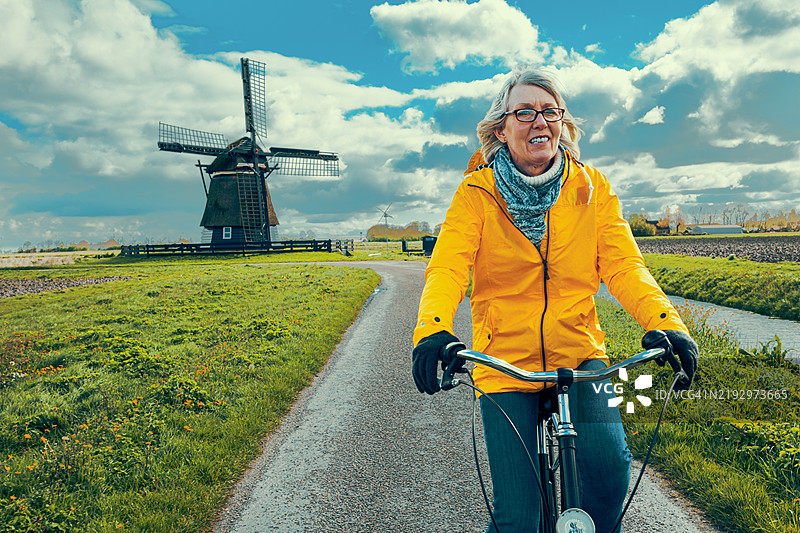 一位老年女性骑自行车经过传统的荷兰风车图片素材