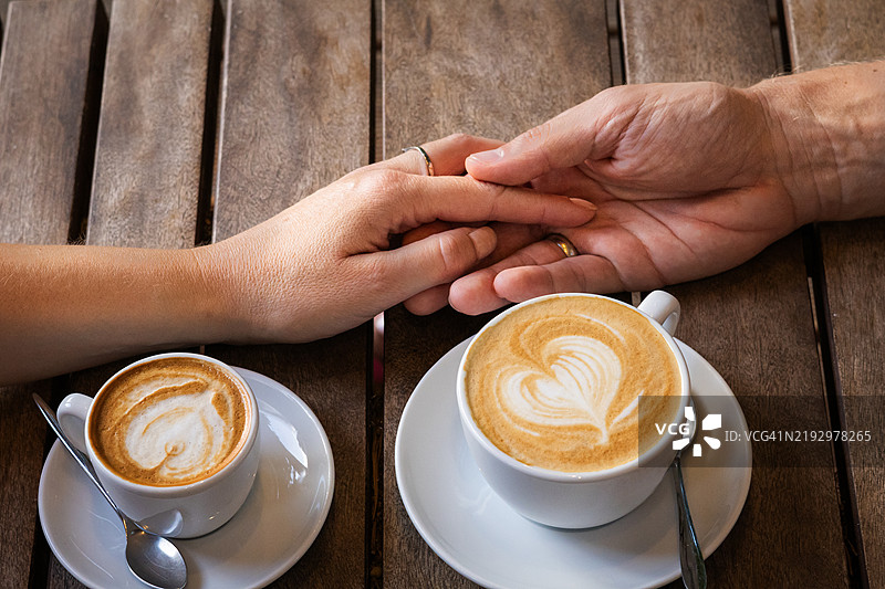 咖啡店复古木桌上的卡布奇诺杯特写。情侣在咖啡休息时相聚。图片素材