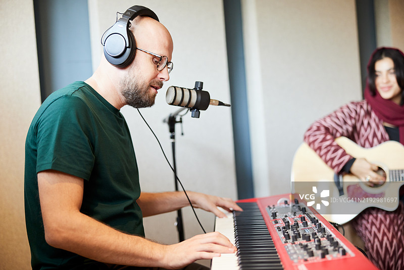一对男女在音响工作室里排练一首歌曲，伴随着吉他和歌声。图片素材