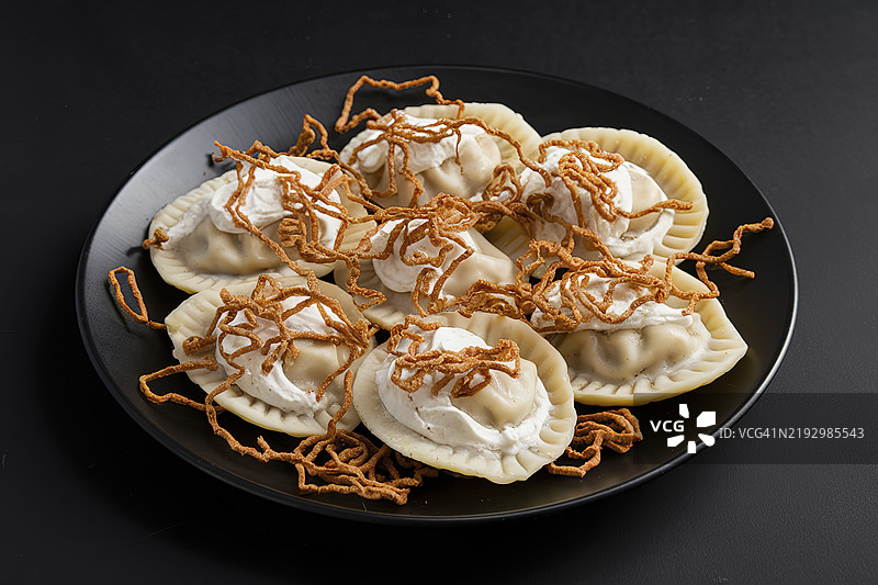 一盘饺子或波兰饺子，配有奶油，点缀脆炸洋葱。图片素材