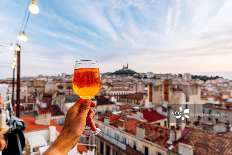男子在屋顶酒吧享用Aperol Spritz鸡尾酒，俯瞰马赛老城，法国蔚蓝海岸。图片素材