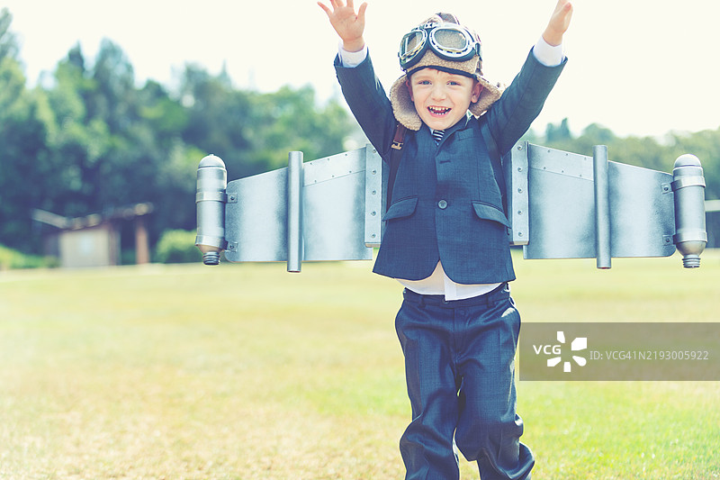 抱负、创新商业理念。一个穿着西装和自制传统飞行员服装的小孩。图片素材