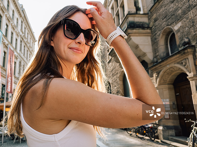 户外美丽时尚女性的肖像。人物佩戴白色智能手表和太阳镜。城市生活概念照片，展示了与友好人群的生活方式摄影。图片素材