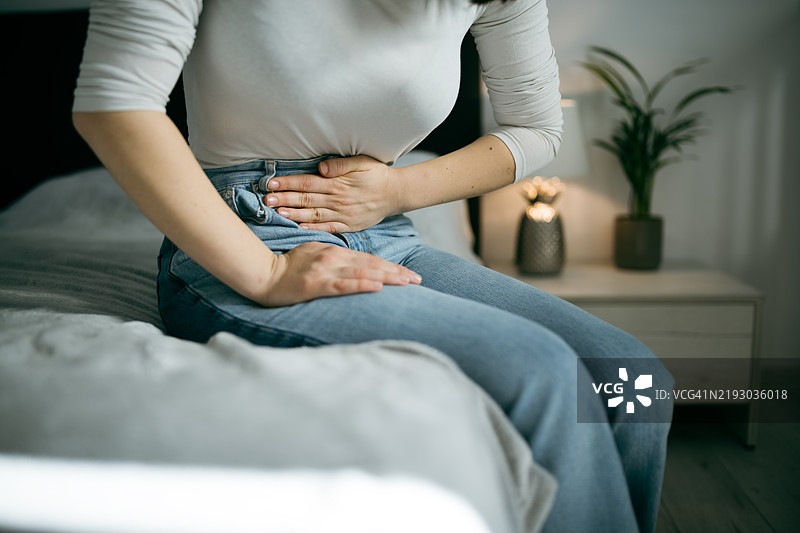 年轻女性正感到腹部不适，双手抱住肚子。图片素材