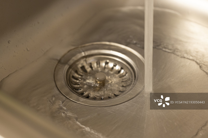厨房水槽的排水口特写，水流倾泻而下。图片素材