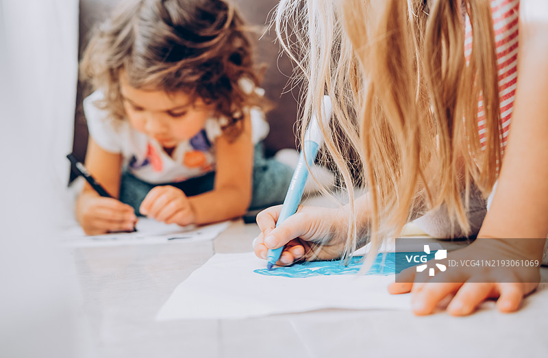 可爱的小女孩们躺在地上用彩色马克笔画画。图片素材