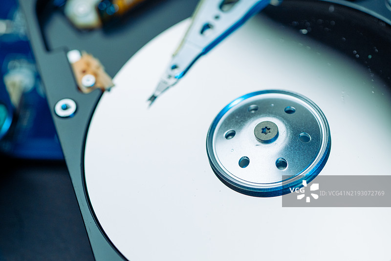 展示打开的硬盘的细节镜头，揭示光亮的盘片、主轴和读写臂。图片素材