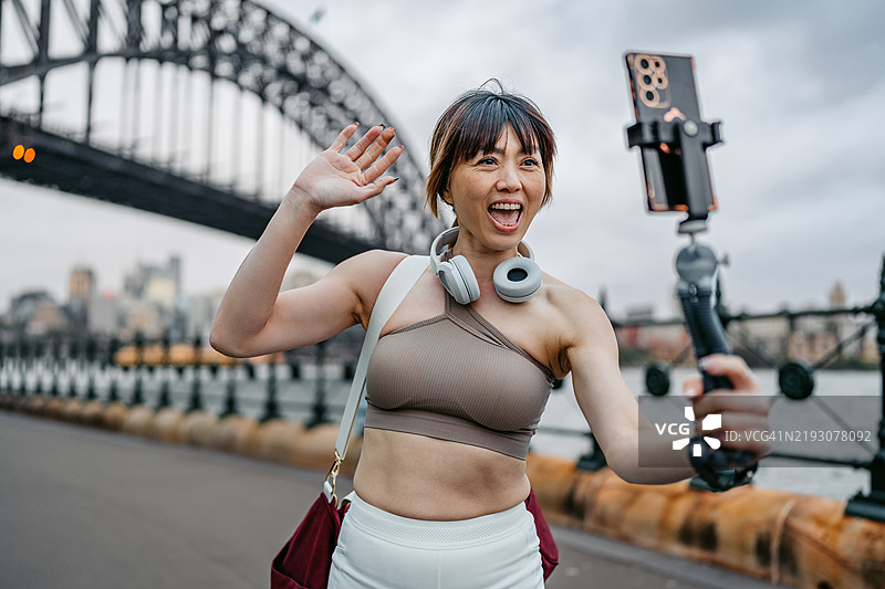 中年华裔女性在澳大利亚悉尼海港大桥附近慢跑后，用手机录制视频博客图片素材