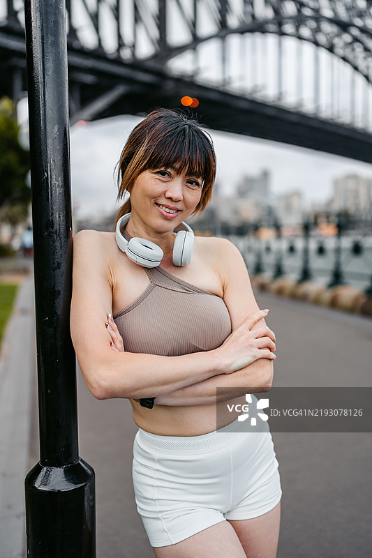 身穿运动服的中年华裔女性站在澳大利亚悉尼的悉尼港大桥附近图片素材