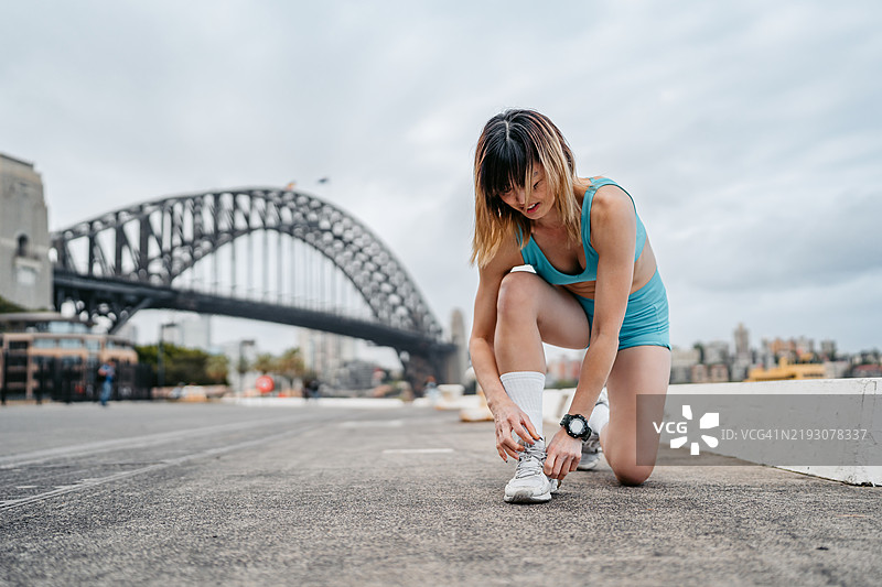中年华裔女性在澳大利亚悉尼海港大桥附近系鞋带准备慢跑图片素材