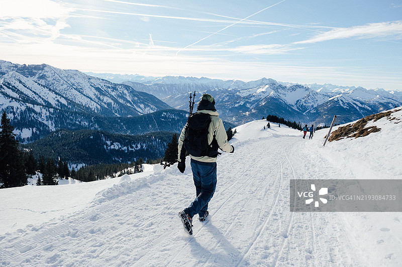 男人们在雪山小道上徒步下山，远处是壮丽的山景图片素材