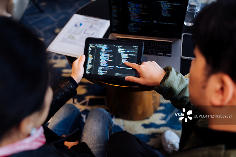 亚洲软件工程师在酒店咖啡厅一起使用平板电脑和笔记本电脑的背影。图片素材