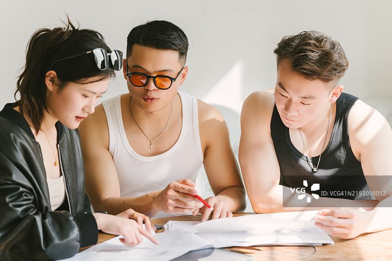 三位来自东亚的年轻人正在研究放在桌子上的蓝图图片素材