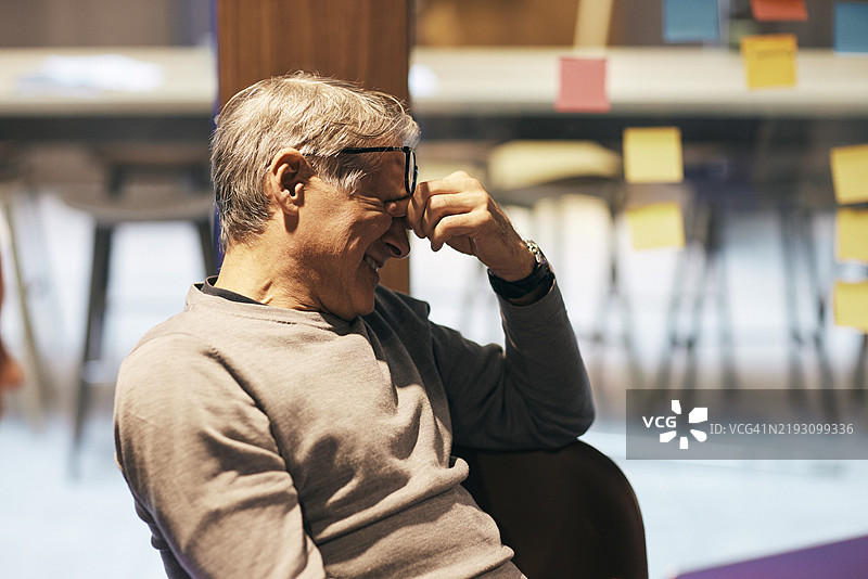 疲惫的老年男性商务专业人士在办公室会议室坐着，揉着眼睛图片素材