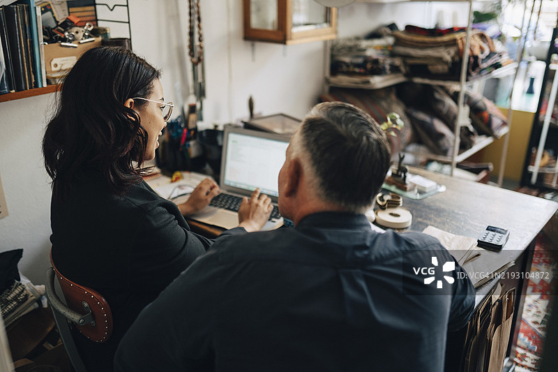 男性店主与女性同事在古董店内使用笔记本电脑的背影图片素材
