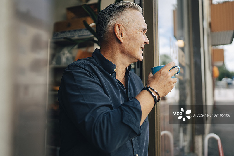 微笑的老年主人手持咖啡杯站在门口图片素材