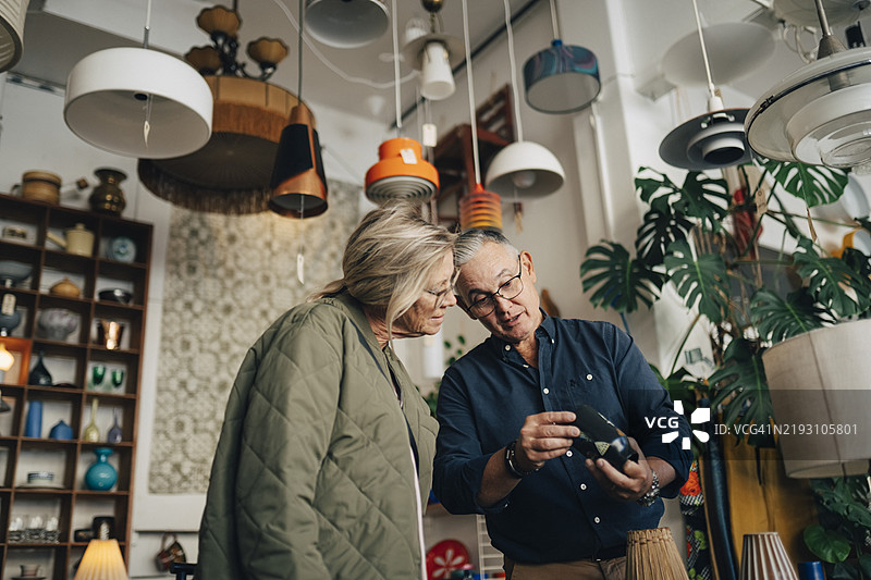低角度视图，老年男性店主在商店里为女性顾客查看花瓶的价格标签图片素材