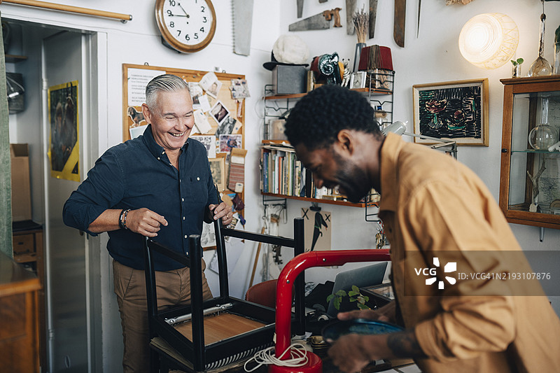 快乐的老年男性店主与顾客在古董店互动图片素材