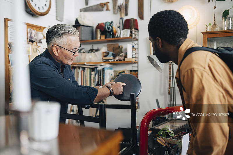 老年男性店主向顾客解释古董店灯具的控制方法图片素材