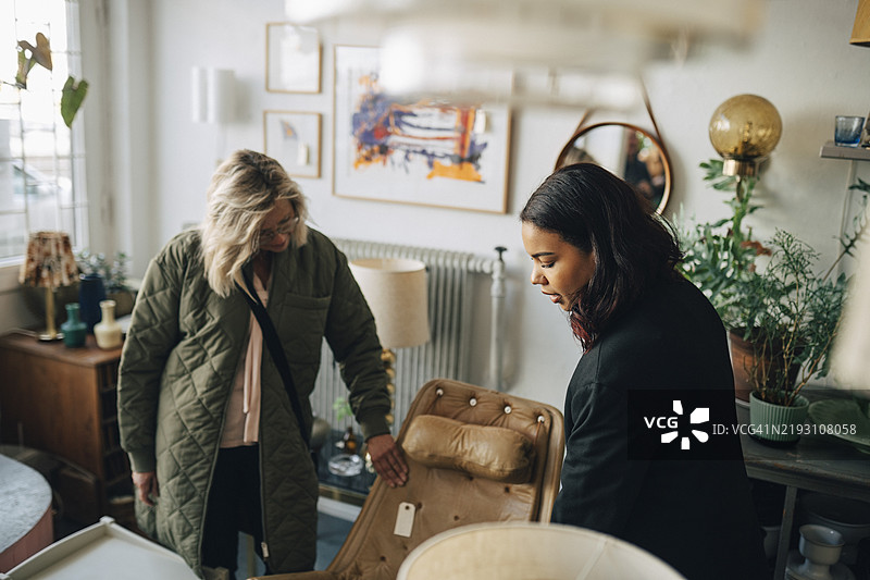 高角度视图的女性店主在古董店帮助顾客购买家具图片素材