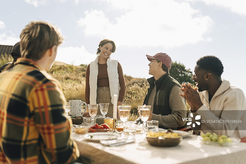 微笑的女性在阳光明媚的日子里与朋友们聚会时站在桌子旁图片素材