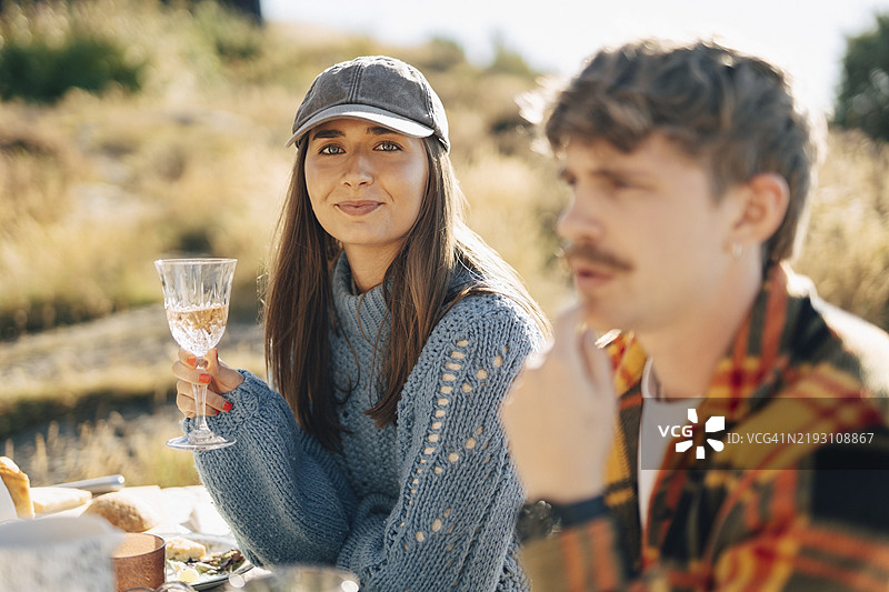 微笑的年轻女性戴着帽子，在晚宴上举着酒杯。图片素材