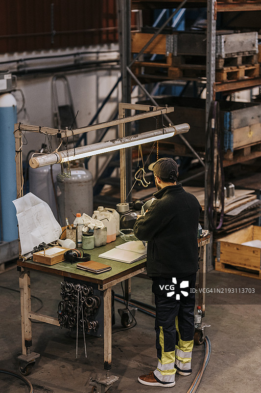 男性工人在工厂中站在桌子旁工作，俯视角度的后视图图片素材