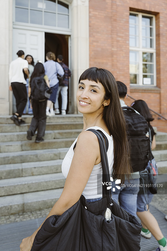 微笑的女性背着包，回头看着大学校园的肖像图片素材