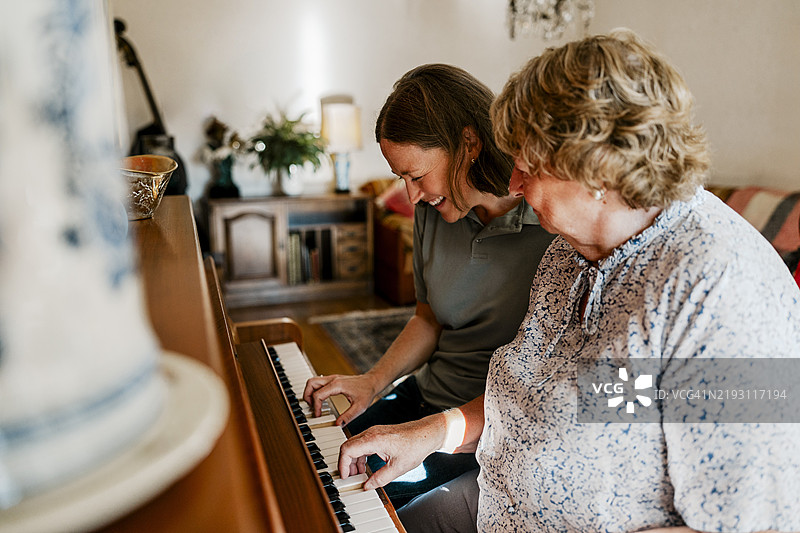 快乐的女护士在家中与老年女性一起弹钢琴图片素材