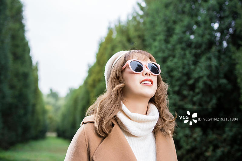 一位年轻女性戴着贝雷帽和太阳镜，正仰望着镜头外的某物。图片素材