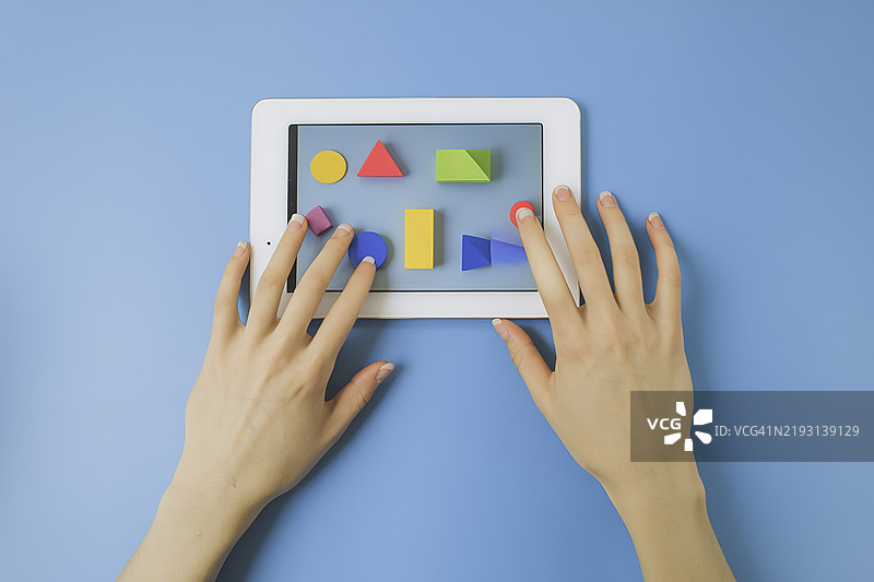 手握平板电脑或智能手机，屏幕上显示着各种多彩的几何图形，背景为蓝色。图片素材