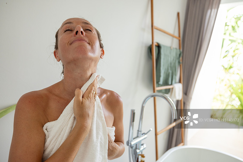 明亮浴室中，女人放松地躺在浴缸里，身上裹着毛巾图片素材
