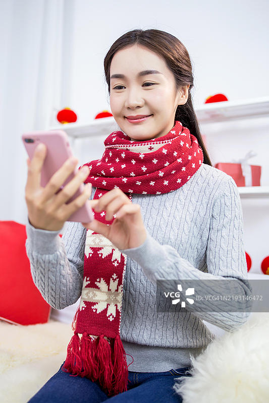 一位年轻女性坐在沙发上使用智能手机。图片素材