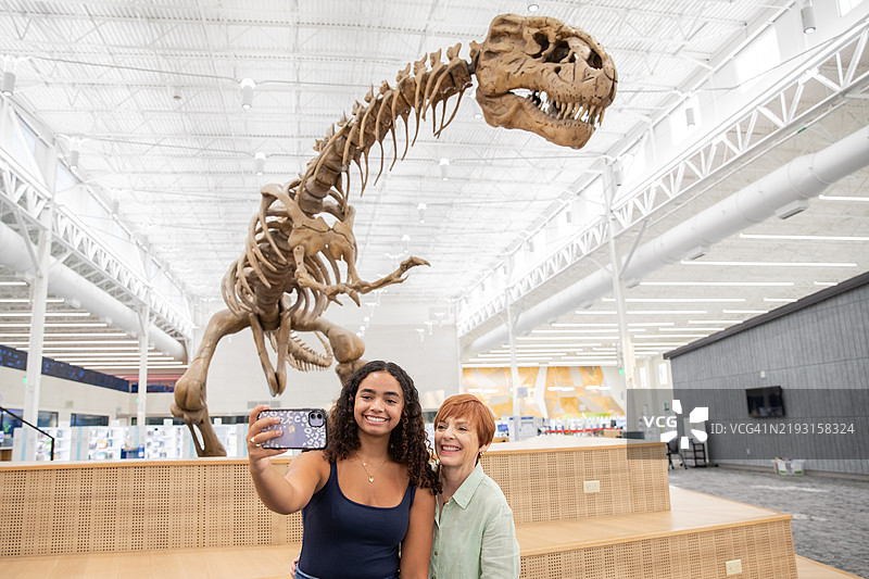 一个少女和她的妈妈在恐龙化石展览前合影自拍。图片素材