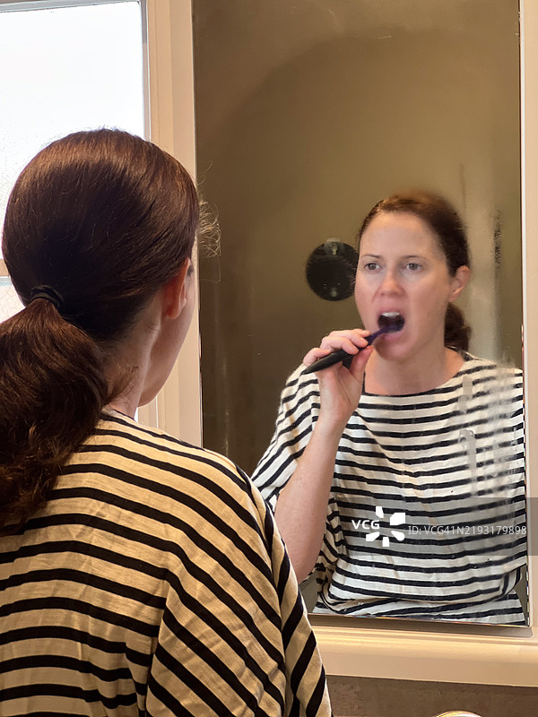 美丽的成年女性在镜子前刷牙时的肖像图片素材