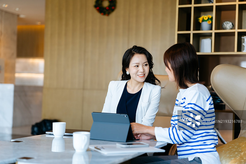 两位女商人在豪华酒店的商务旅行中使用数字平板电脑工作和讨论。图片素材