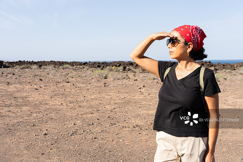女性徒步旅行者在探索兰萨罗特的火山地形时用手遮住眼睛以抵挡阳光图片素材