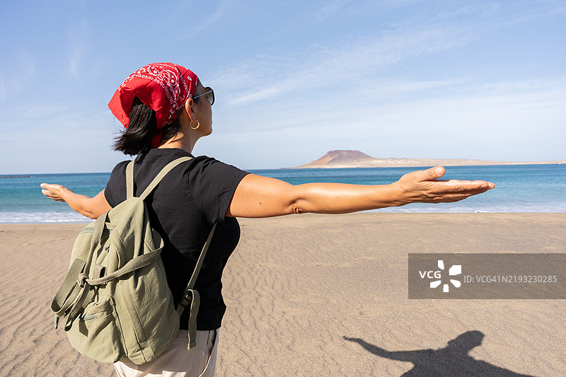 女性游客在西班牙加那利群岛兰萨罗特的海滩上张开双臂享受自由图片素材