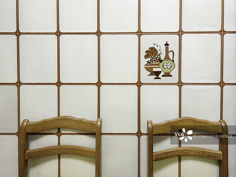 1980年代厨房中带有复古装饰的瓷砖墙旁的两把椅子图片素材