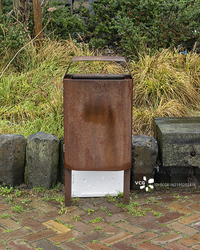 生锈的钢制垃圾桶位于一排石块前面。图片素材