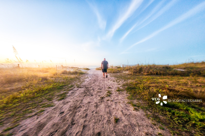 中年男子沿着沙滩小路走向海滩图片素材