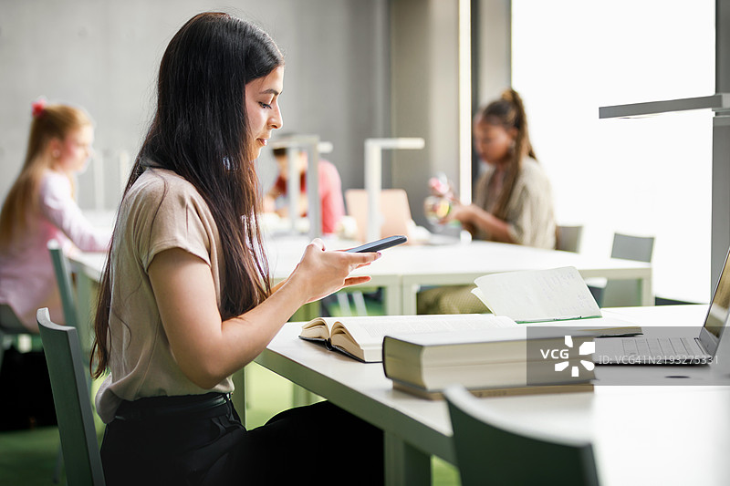年轻女学生在图书馆学习时使用智能手机图片素材