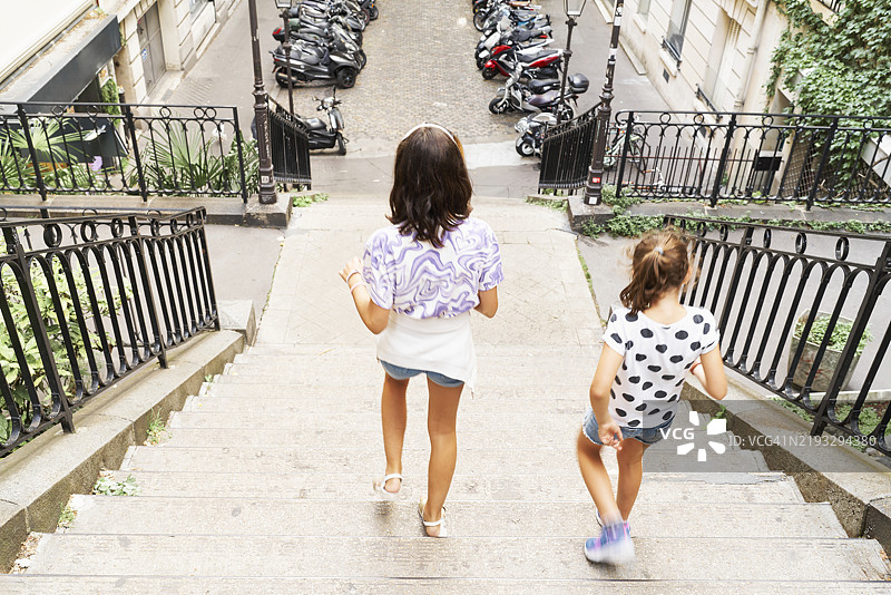 两个穿着休闲服的女孩从街道楼梯上一起走下来的背影图片素材