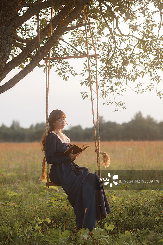 年轻女性在乡村秋千上阅读图片素材
