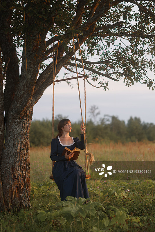 年轻女性在乡村秋千上阅读图片素材