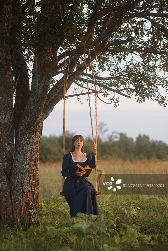 年轻女性在乡村秋千上阅读图片素材
